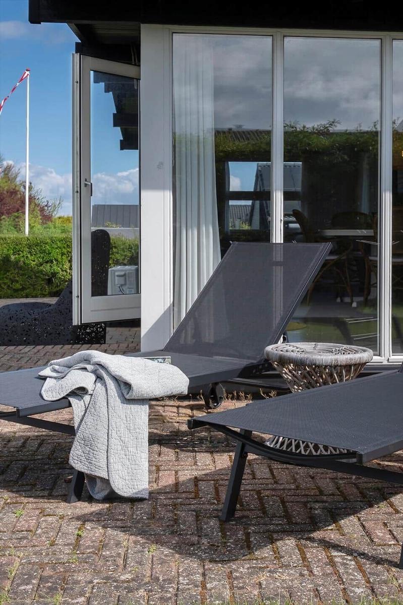Terrasse mit Liegestühlen und Blick ins Haus. Graue Decke liegt auf einem Stuhl.