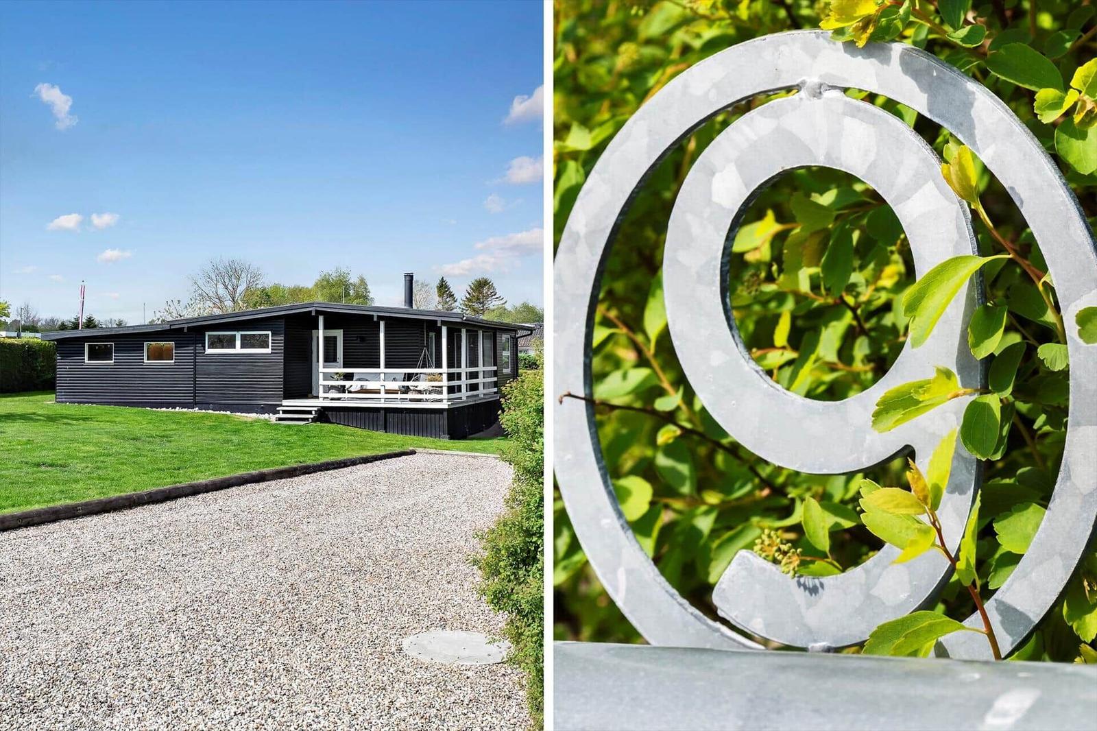 Schwarzes Haus mit Terrasse und grünem Garten. Metall-Symbol im Busch.