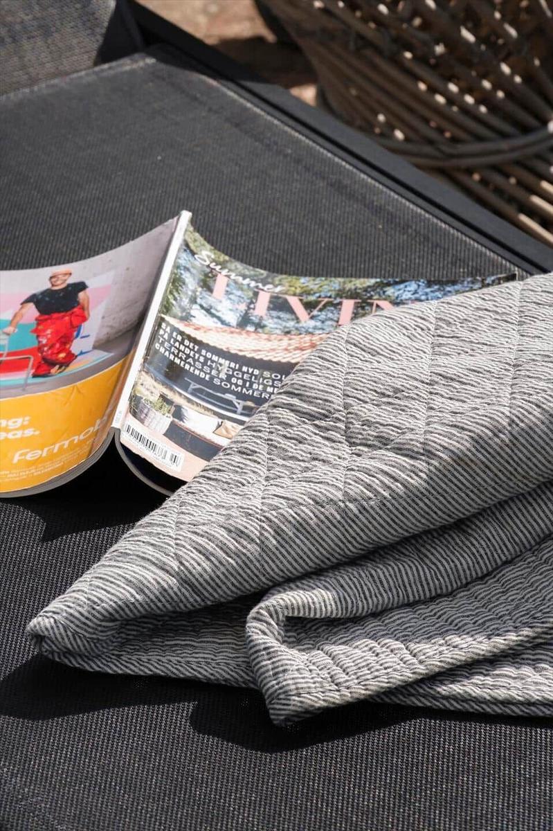 Zwei Zeitschriften und eine gestreifte Decke liegen auf einer Außenterrassenbank.