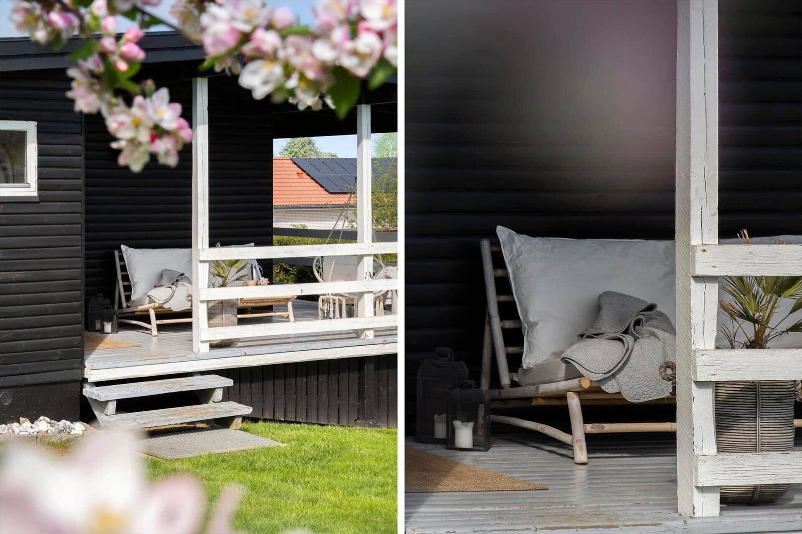 Terrasse mit Liegestuhl, Kissen und Decke. Schwarze Fassade, weiße Holzstrukturen und grüner Rasen.