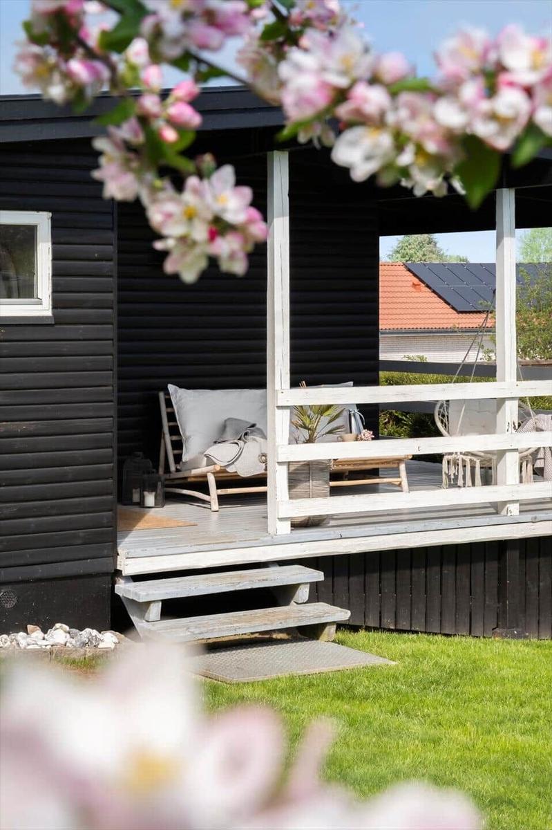 Terrasse mit Liegestuhl und Blumen vor schwarzem Holzhaus