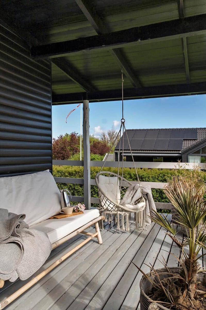 Terrasse mit Hängesessel, Sofa und Pflanze. Blick auf Garten und Nachbarhaus.
