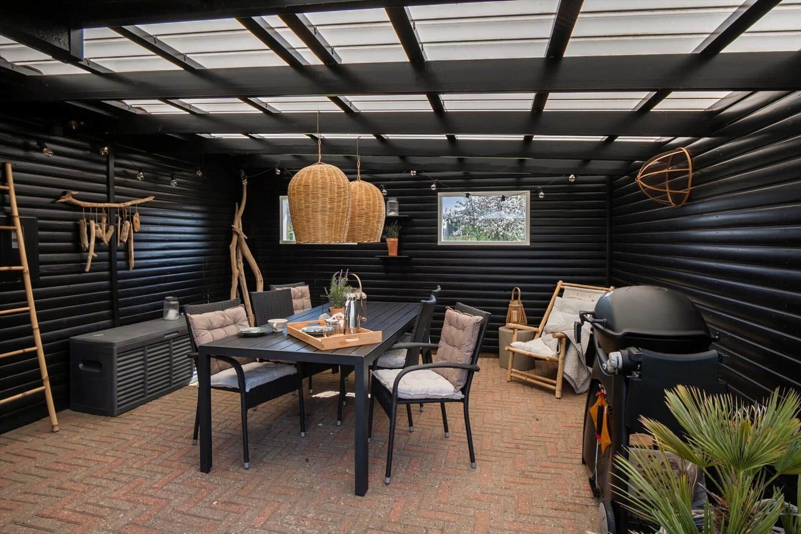 Terrasse mit Tisch, Stühlen, Grill und Hängelampe unter schwarzem Dach.
