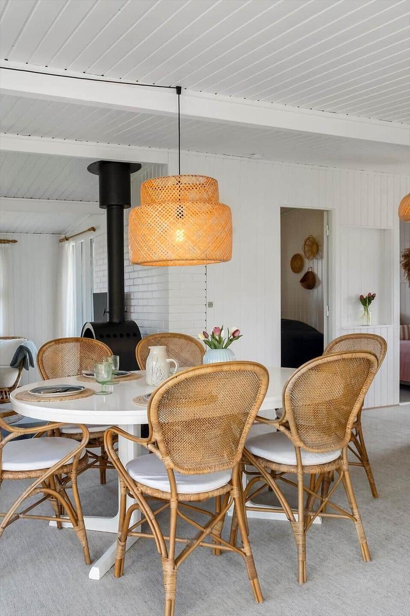 Rattan-Stühle um einen runden Tisch mit Decken und Vasen. Hängelampe und Kamin im Hintergrund.