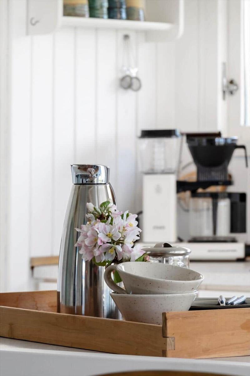 Küchenbereich mit Thermoflasche, Tassen und Blumen auf Holztablett.