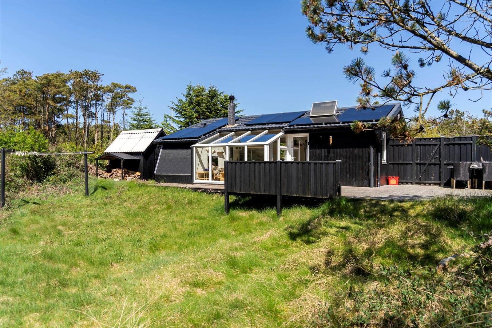 Schwarzes Haus mit Solaranlage und Terrasse im Grünen.