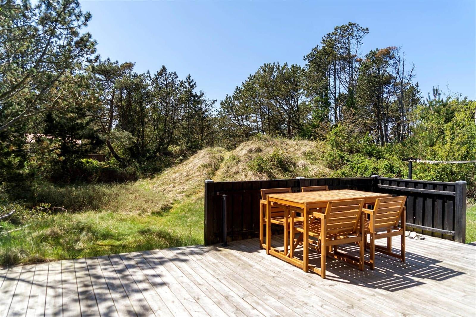Holzterrasse mit Tisch und Stühlen. Blick auf grüne Wiesen und Bäume.