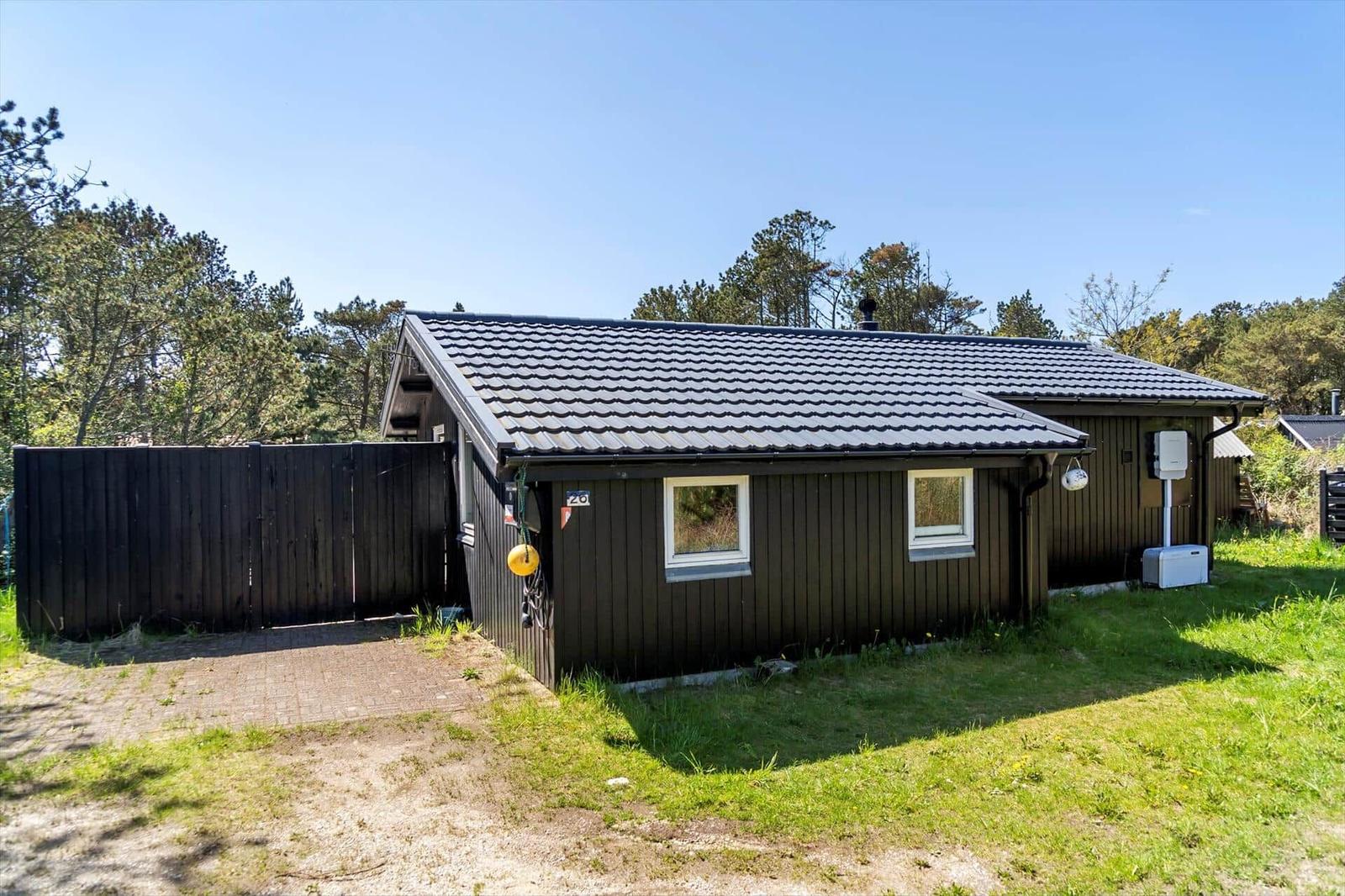 Holzhaus mit Dach und zwei Fenstern, umgeben von Gras und Bäumen.