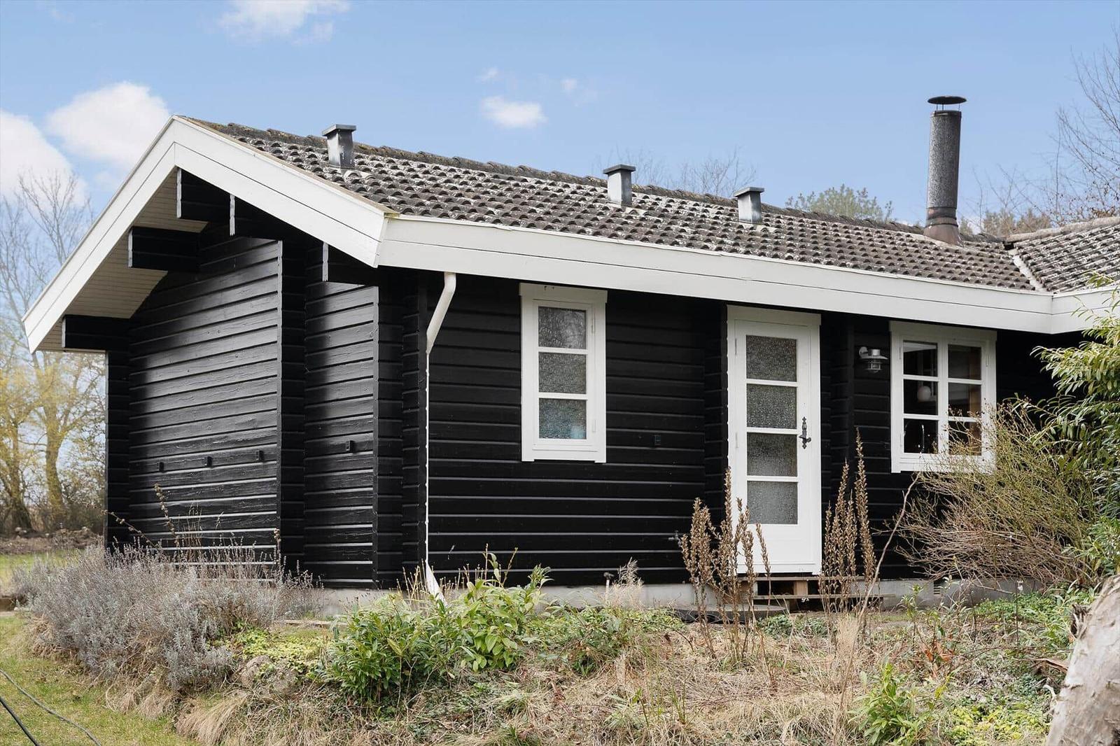 Black wooden house with white windows and door under blue sky.
