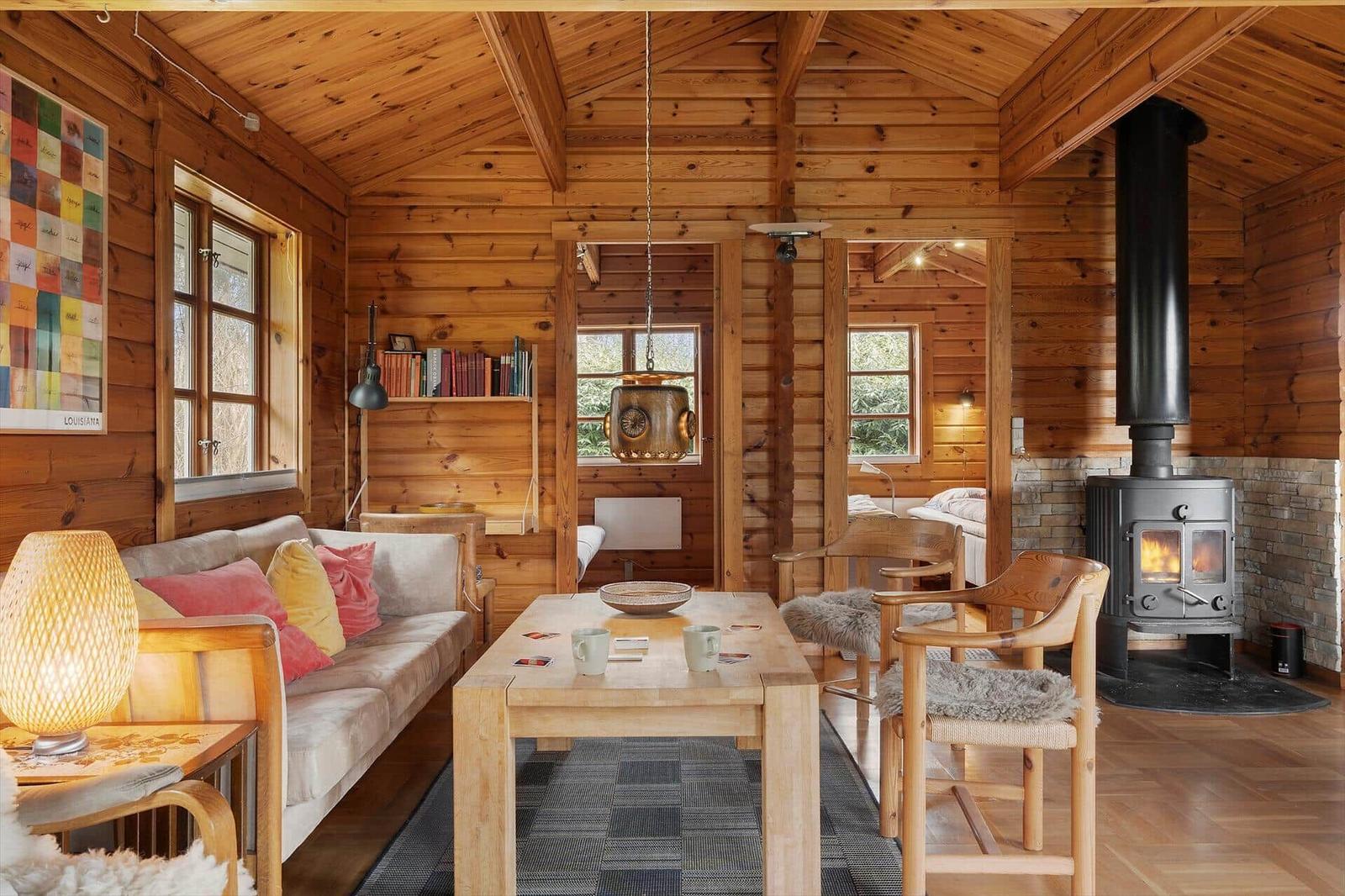 Wooden house with sofa, table, chairs, and wood stove. Windows and bookshelf visible.