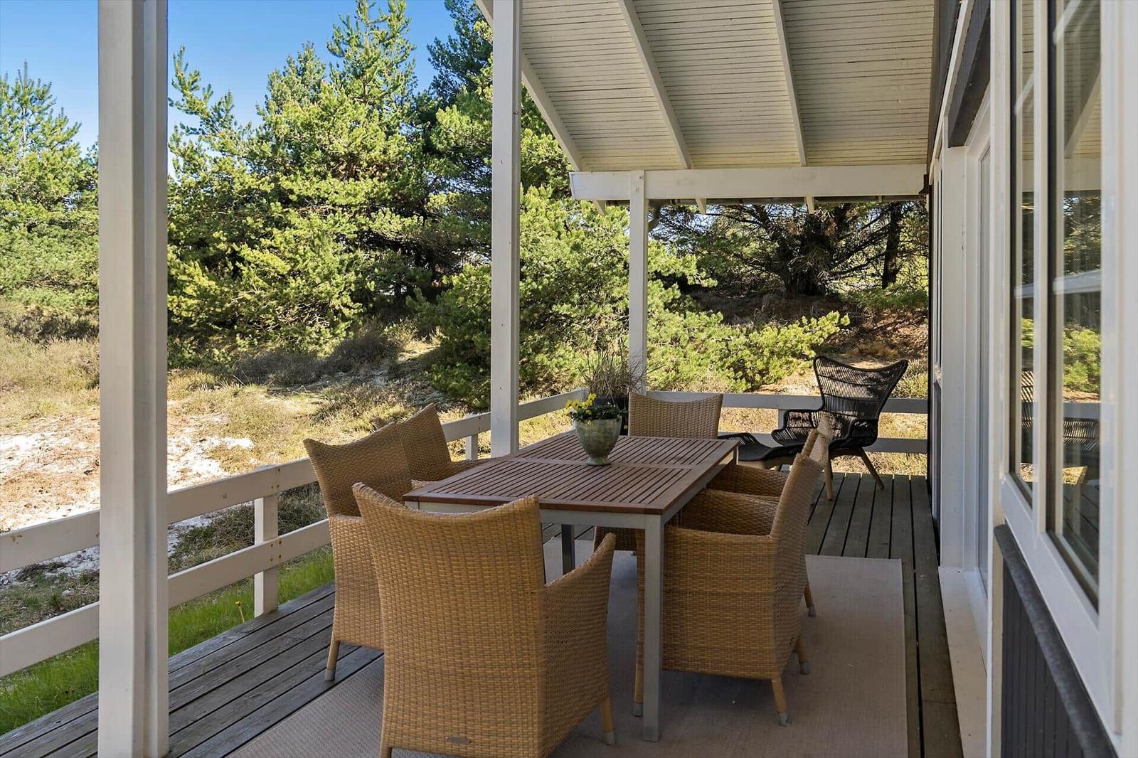 Terrasse mit Tisch und Stühlen, Blick auf Bäume und Gras.