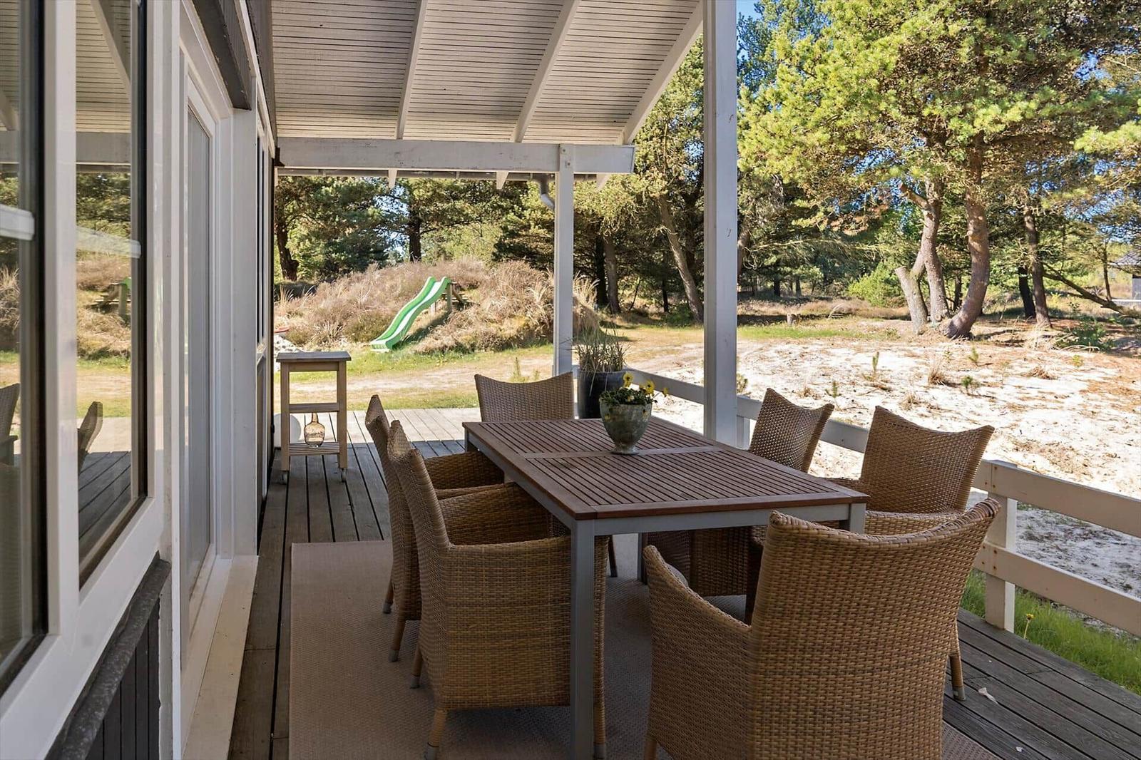 Terrasse mit Tisch und Stühlen, Blick auf Wald und Sandstrand.