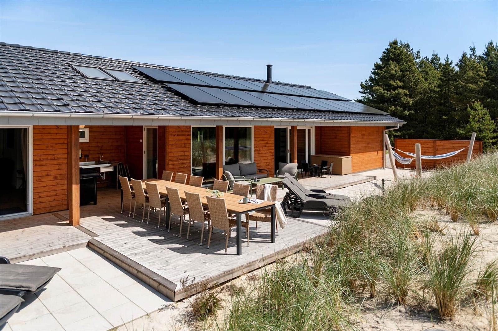 Holzhaus mit Terrasse, Esstisch, Liegestühlen und Hängematten im Strandbereich.