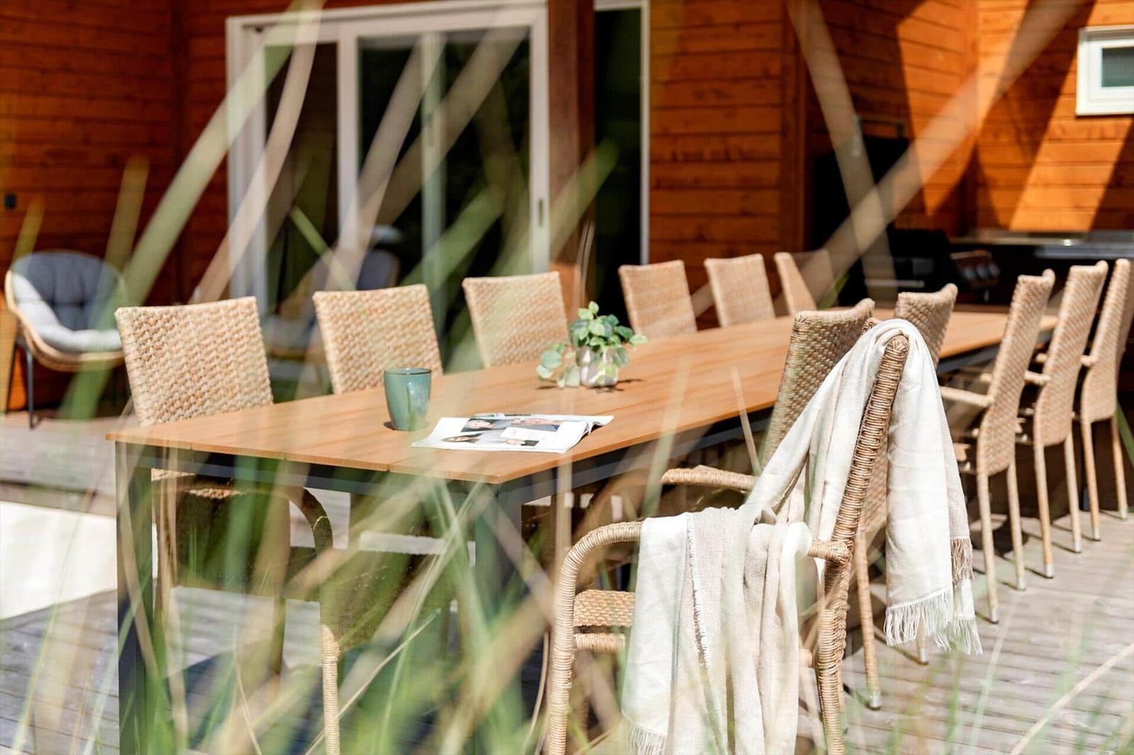 Lange Holzterrasse mit Esstisch und Stühlen, Blick auf Holzhaus im Hintergrund.