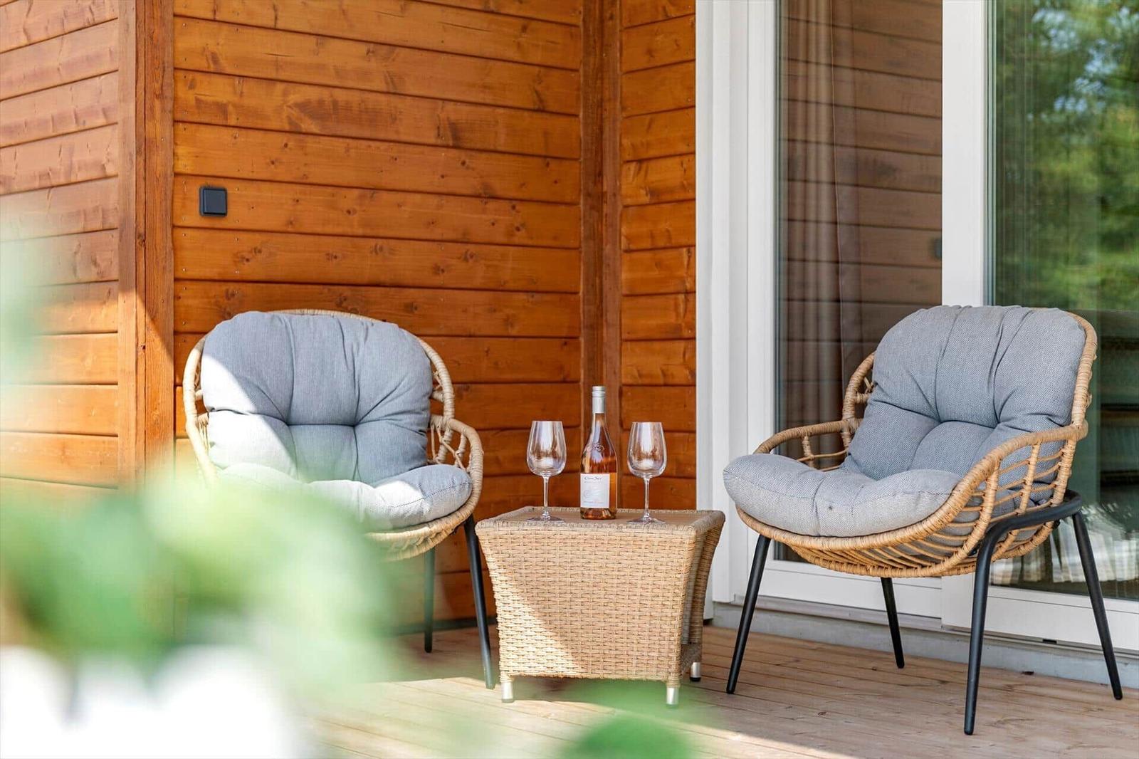 Zwei Sessel mit Kissen und Tisch mit Weinflasche auf Terrasse.