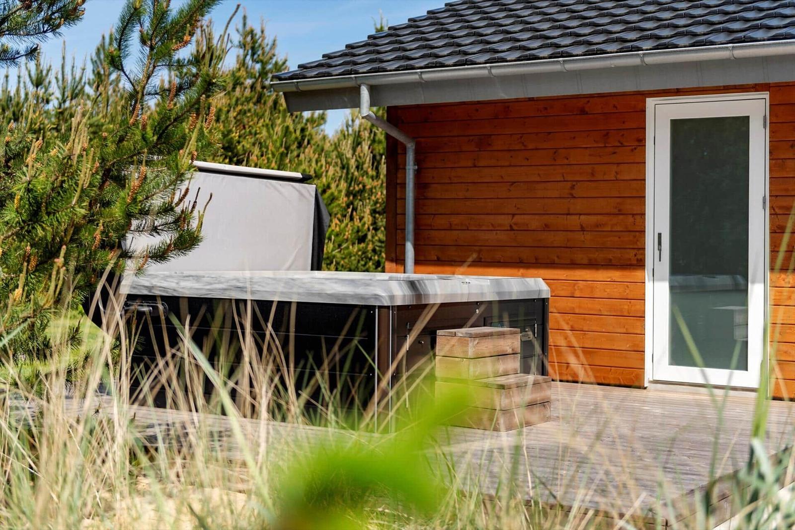 Haus mit Holzwand, Terrasse und Whirlpool im Garten.