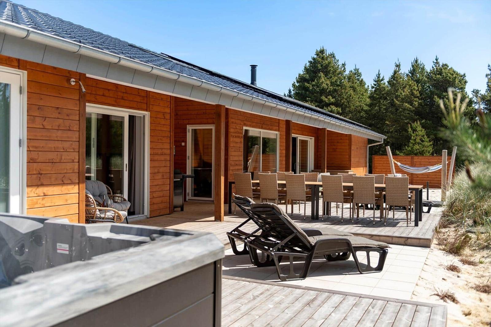 Holzhaus mit Terrasse, Liegen, Tisch und Stühlen sowie Whirlpool im Vordergrund.