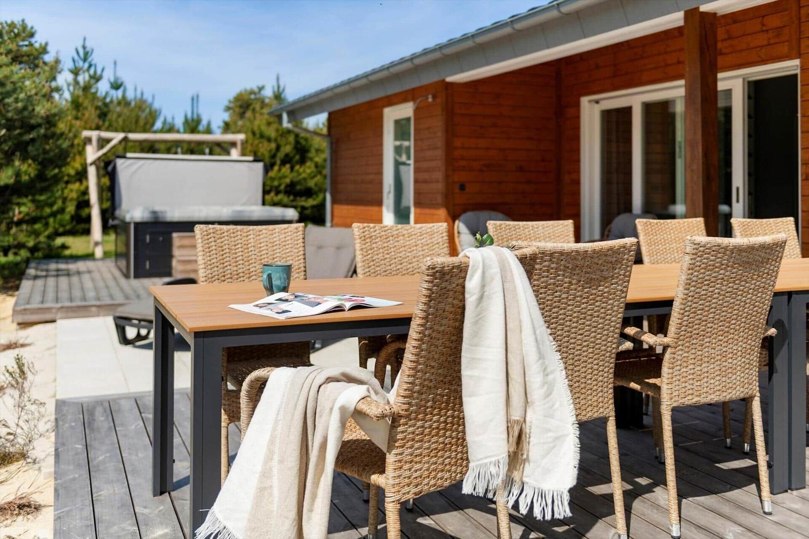 Terrasse mit Esstisch, Stühlen und Decken. Hintergrund: Holzhaus und Grillbereich.