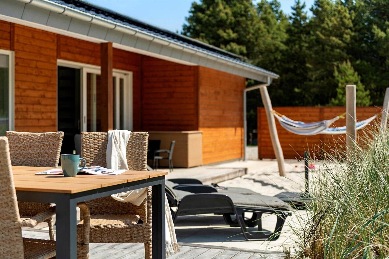 Terrasse mit Tisch, Stühlen, Liegen und Hängematten vor Holzhäusern.