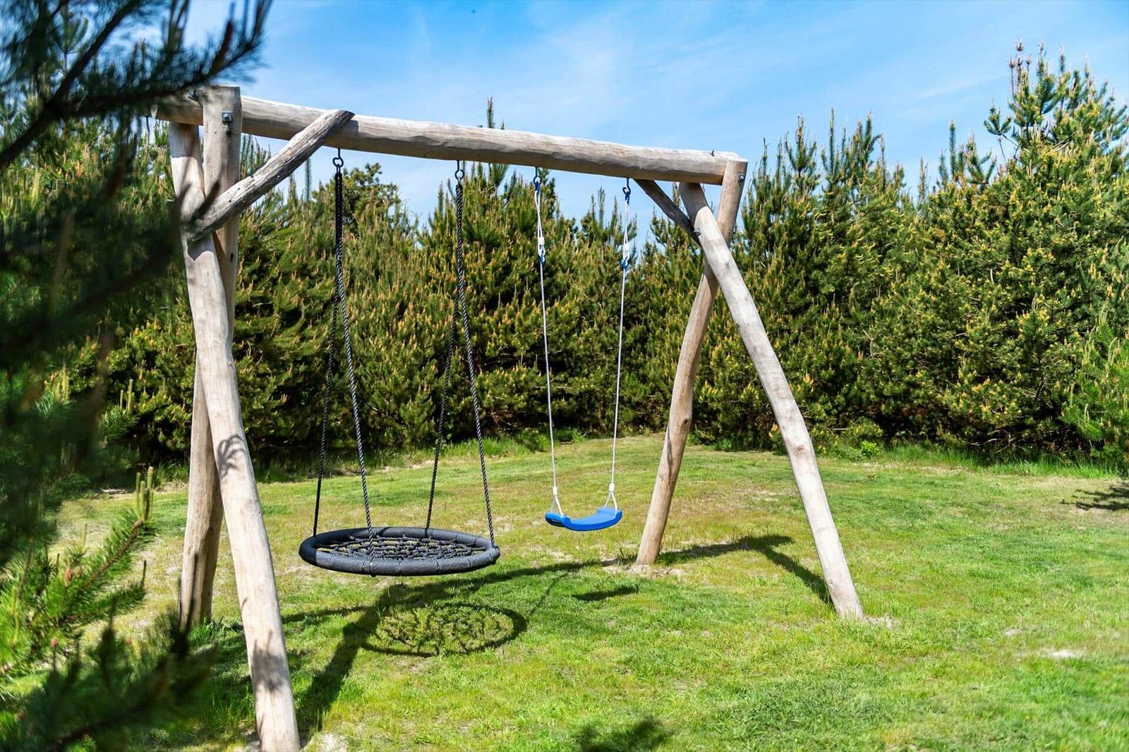 Hölzerne Schaukel mit Rundschaukel und blauer Sitzschaukel im Gras.