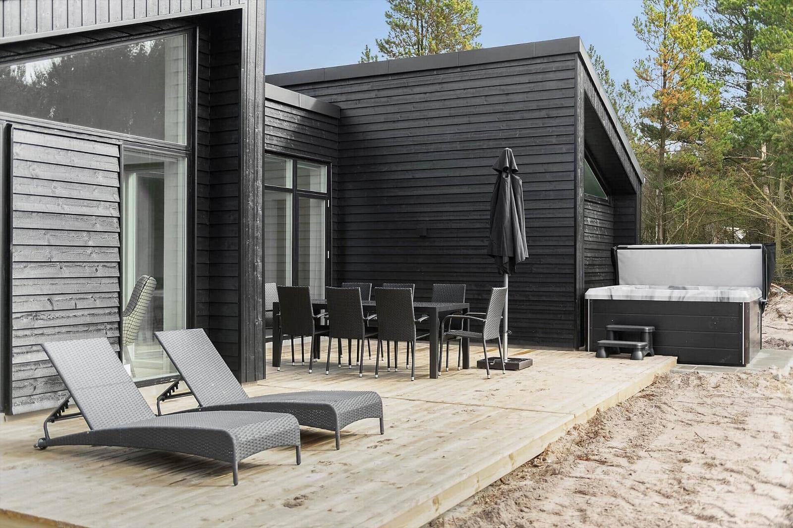 Terrasse mit Liegestühlen, Tisch, Stühlen und Whirlpool neben modernem Haus.