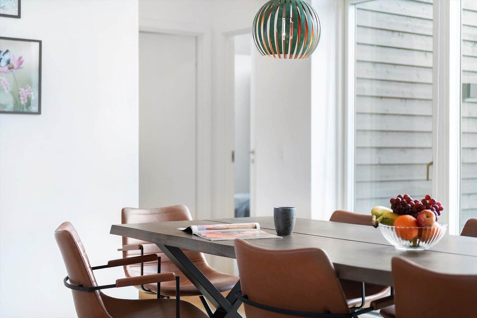 Esstisch mit braunen Stühlen und Obstschale unter einer Lampe.