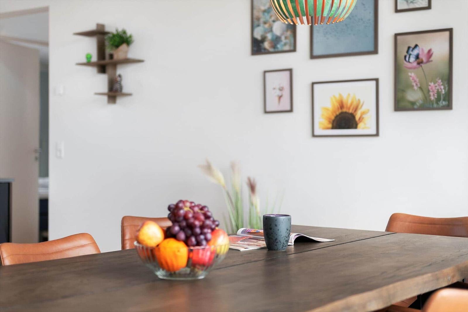 Esszimmer mit Holztisch, Obstschale und Wandbildern.