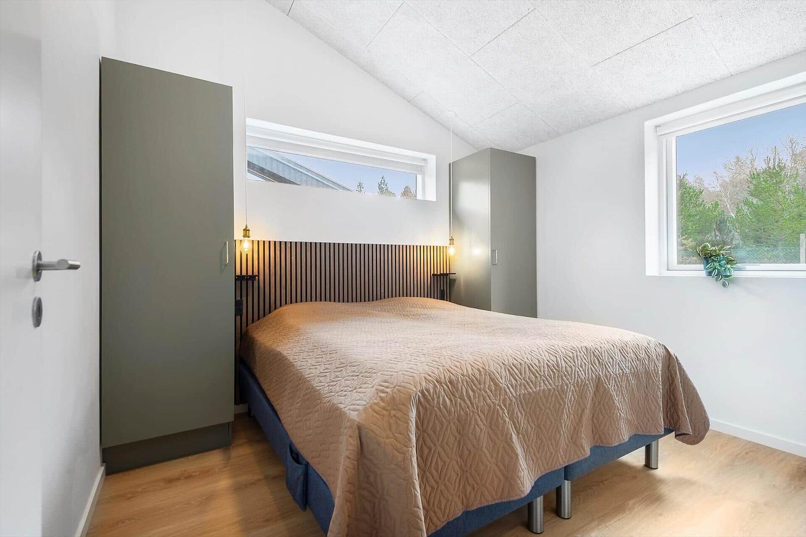 Schlafzimmer mit Bett, Kleiderschrank und Fenster mit Blick auf Bäume.
