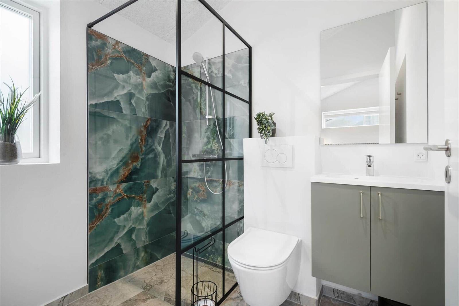 Badezimmer mit Dusche, Toilette und Waschbecken. Duschwand aus grünem Marmor.
