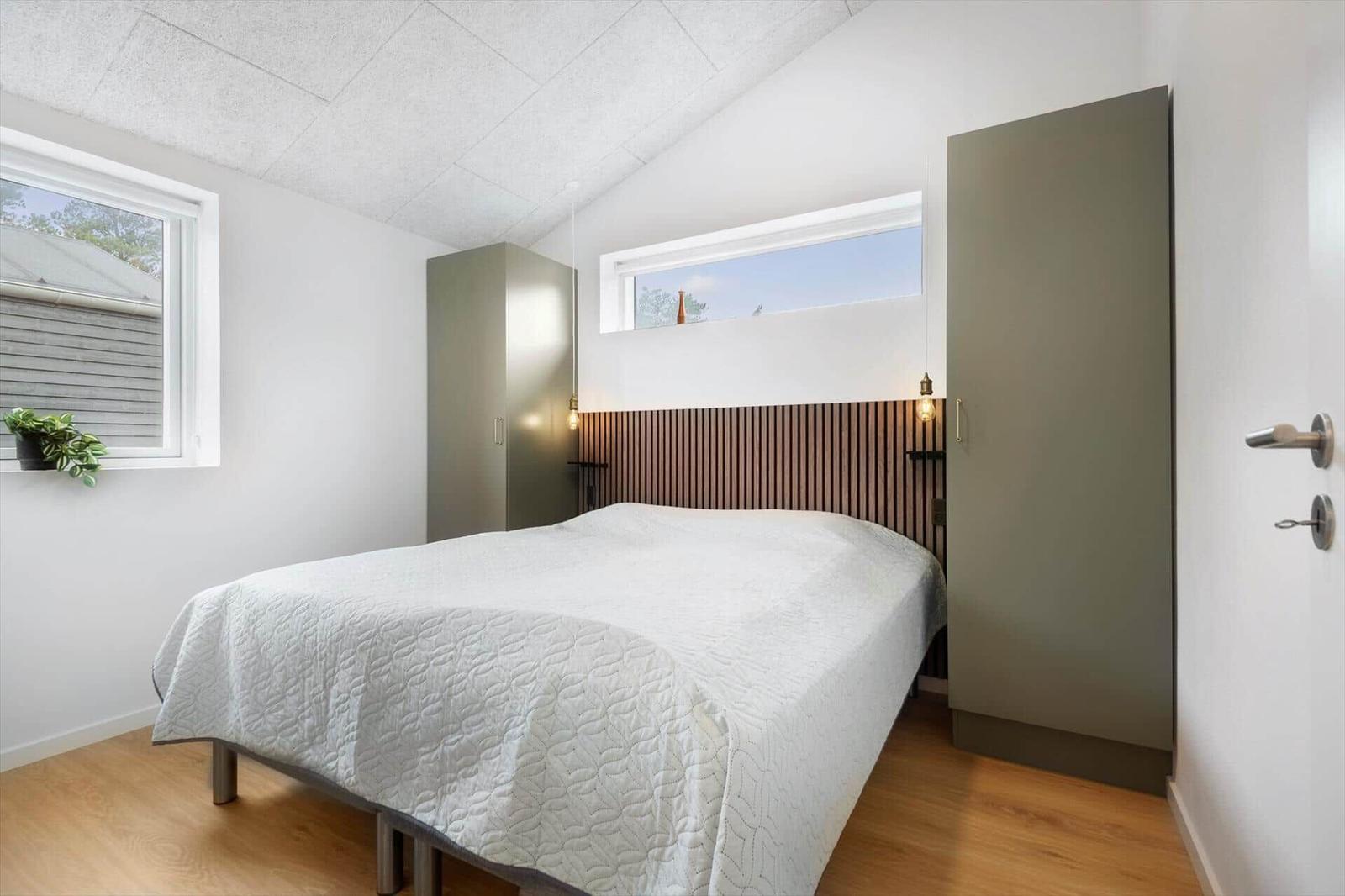 Schlafzimmer mit Bett, Holzfußboden und zwei Fenstern. Zwei Schränke an den Wänden.