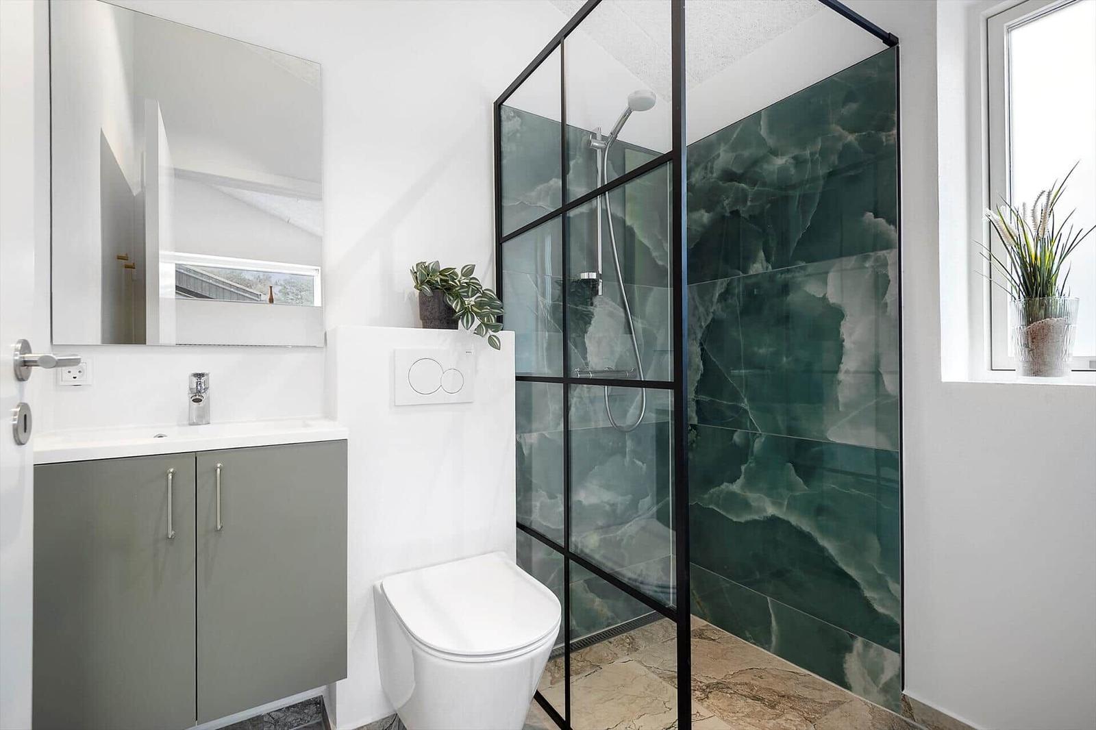 Badezimmer mit Dusche, Waschbecken und Toilette. Grün gemasertes Mosaik an der Wand.