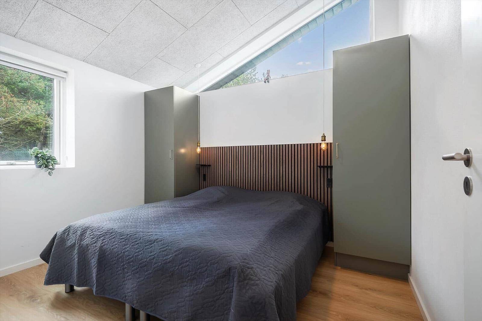 Schlafzimmer mit Bett, Holzfußboden und großen Fenstern.