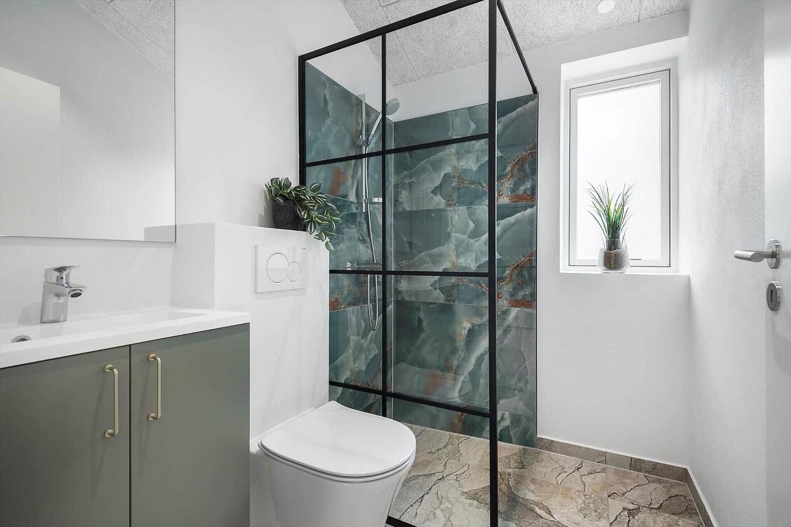 Badezimmer mit Dusche, Waschbecken und Toilette. Fenster mit Pflanze.