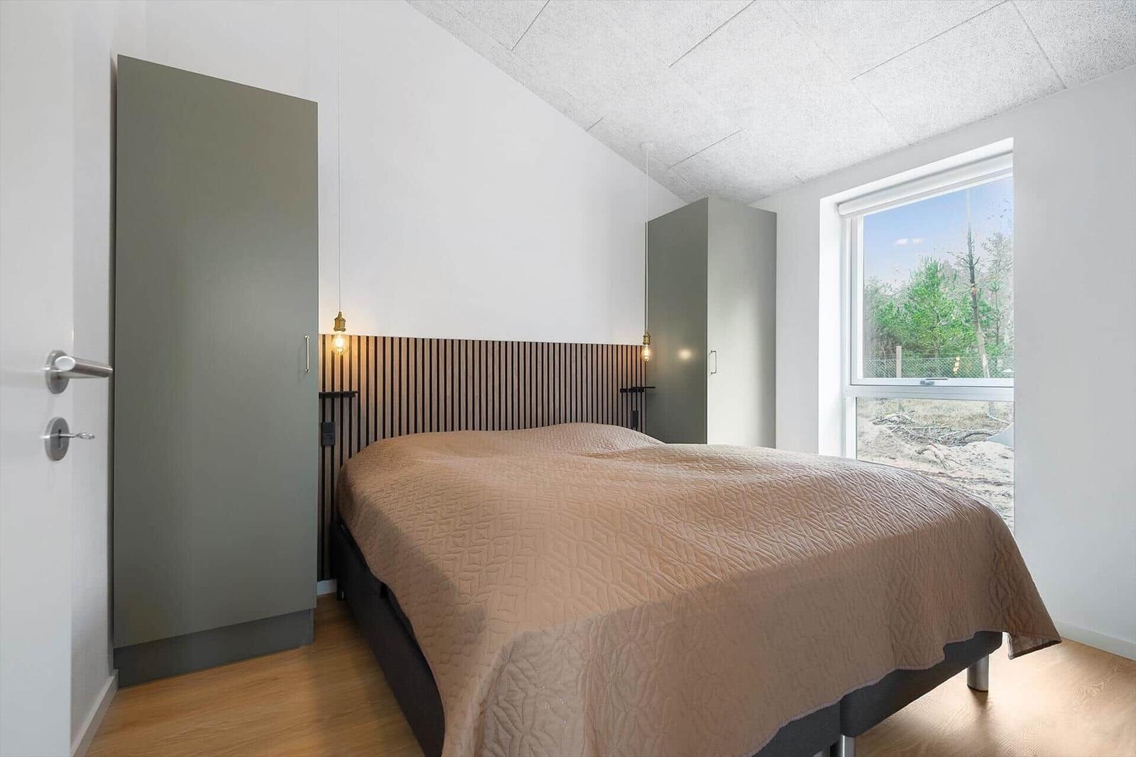 Schlafzimmer mit Bett, Kleiderschrank und Fenster mit Blick auf Wald.