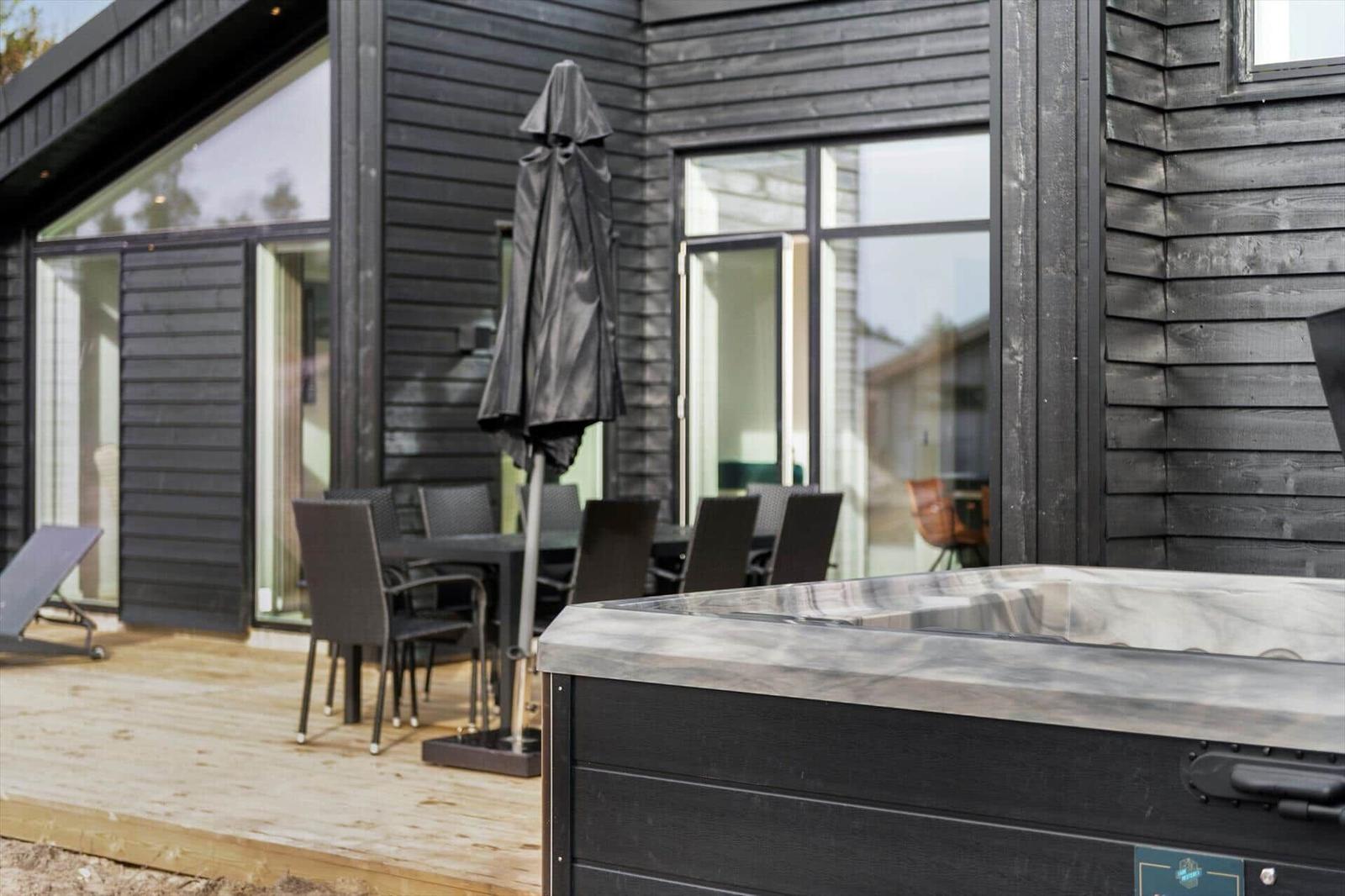 Außenbereich mit Whirlpool, Tisch und Stühlen vor einem Haus mit dunklem Holzverkleidung.