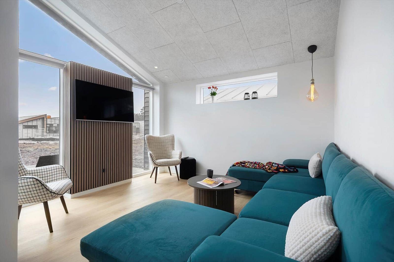 Ein Wohnzimmer mit blauem Sofa, Fernseher und großem Fenster. Helle Wände und Holzboden.
