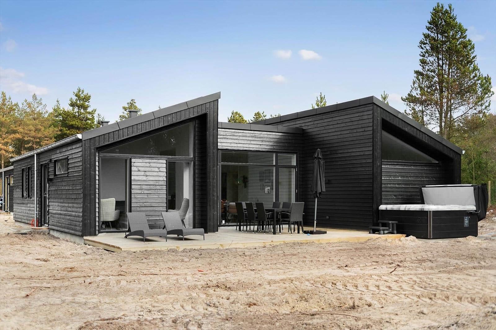 Moderne Holzhütte mit Terrasse, Grillplatz und Whirlpool im Wald.