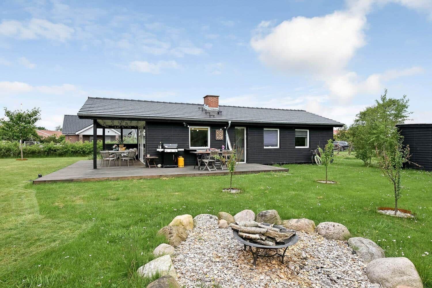 Schwarzes Haus mit Terrasse, Grill und Feuerkorb im Garten.