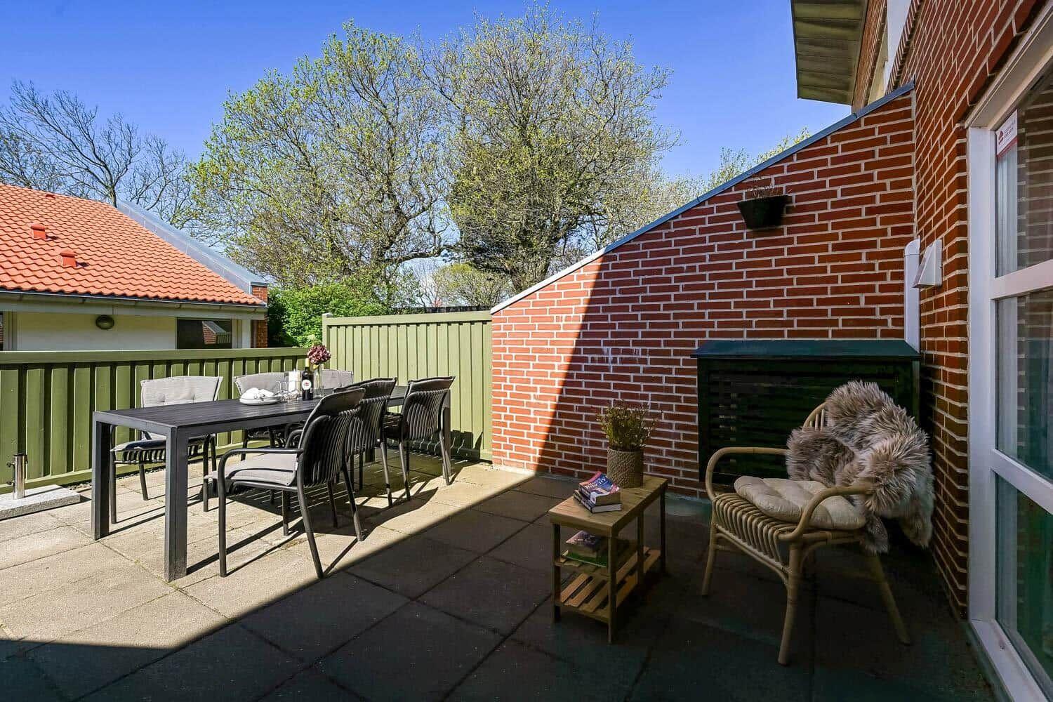 Terrasse mit Esstisch, Stühlen und Sitzgelegenheit an Backsteinwand.
