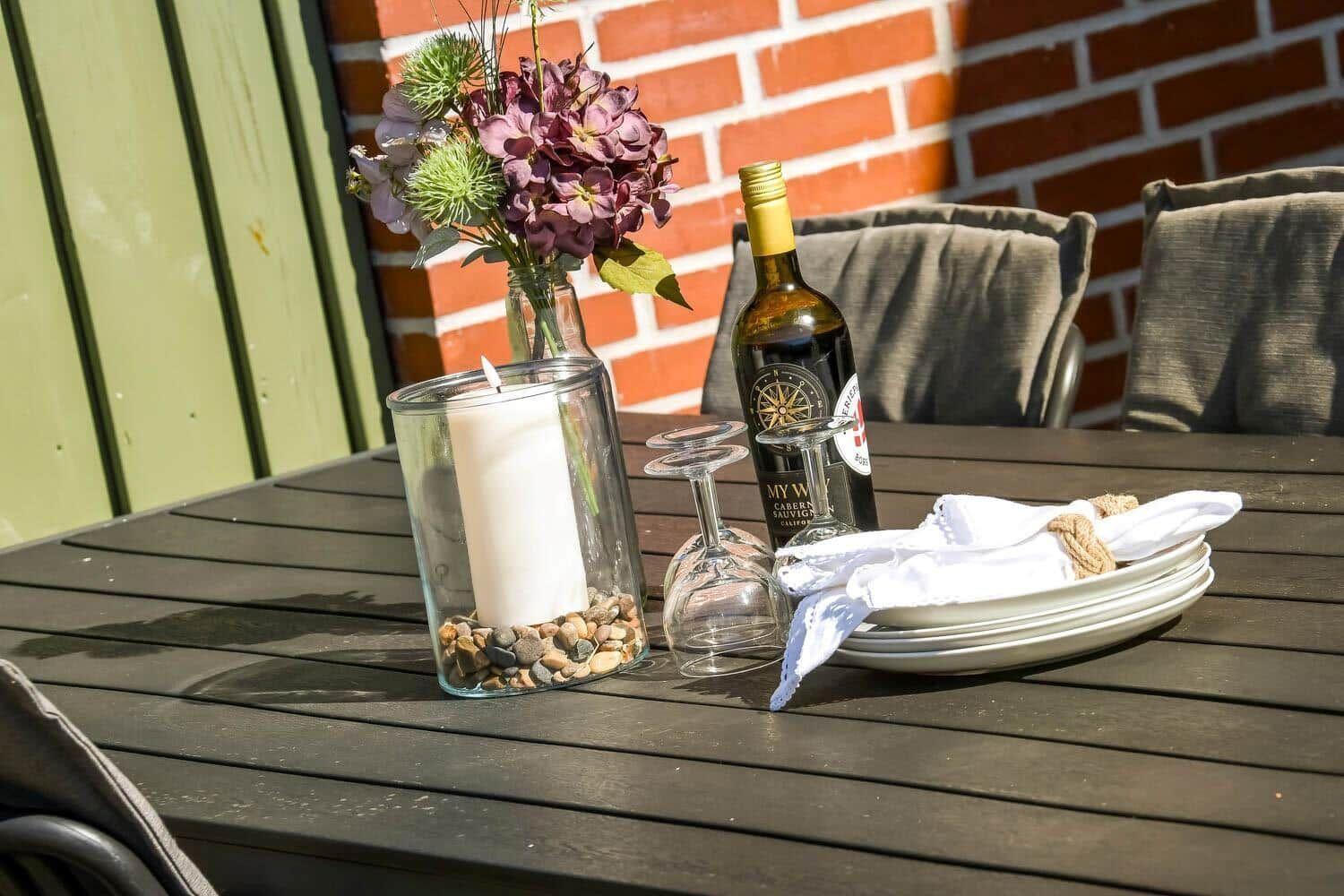 Außenbereich mit Tisch, Stühlen, Blumen, Kerze und Weinflasche.