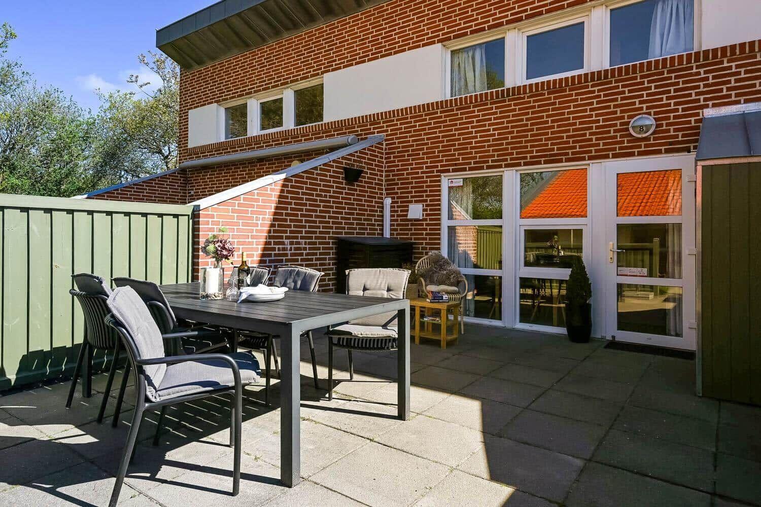 Terrasse mit Tisch, Stühlen und Sitzgelegenheit vor einem Backsteinhaus mit Eingangstür.