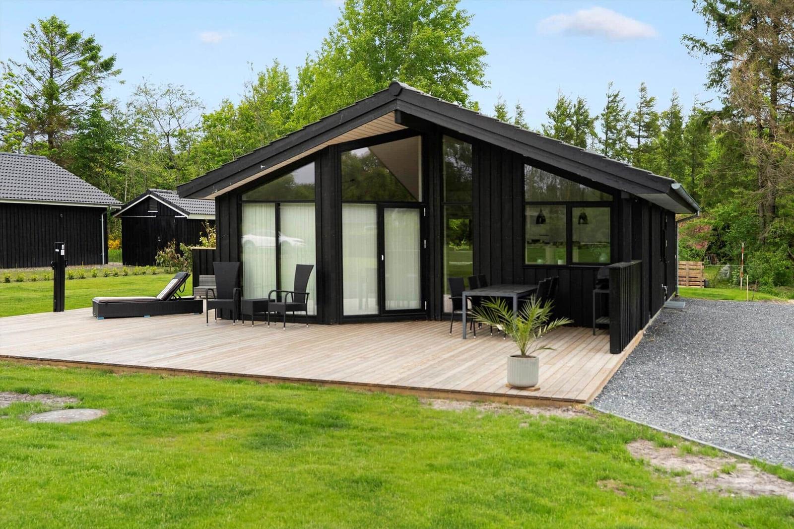 Modern wooden cabin with large deck, garden, and seating areas.