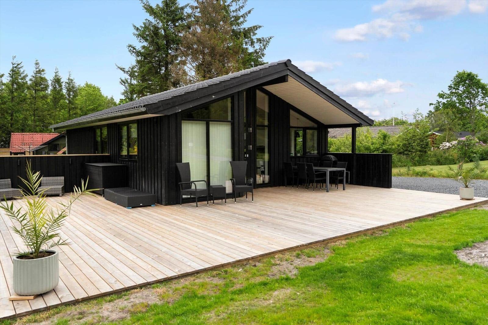 Modern wooden cabin with large deck, seating, and garden.