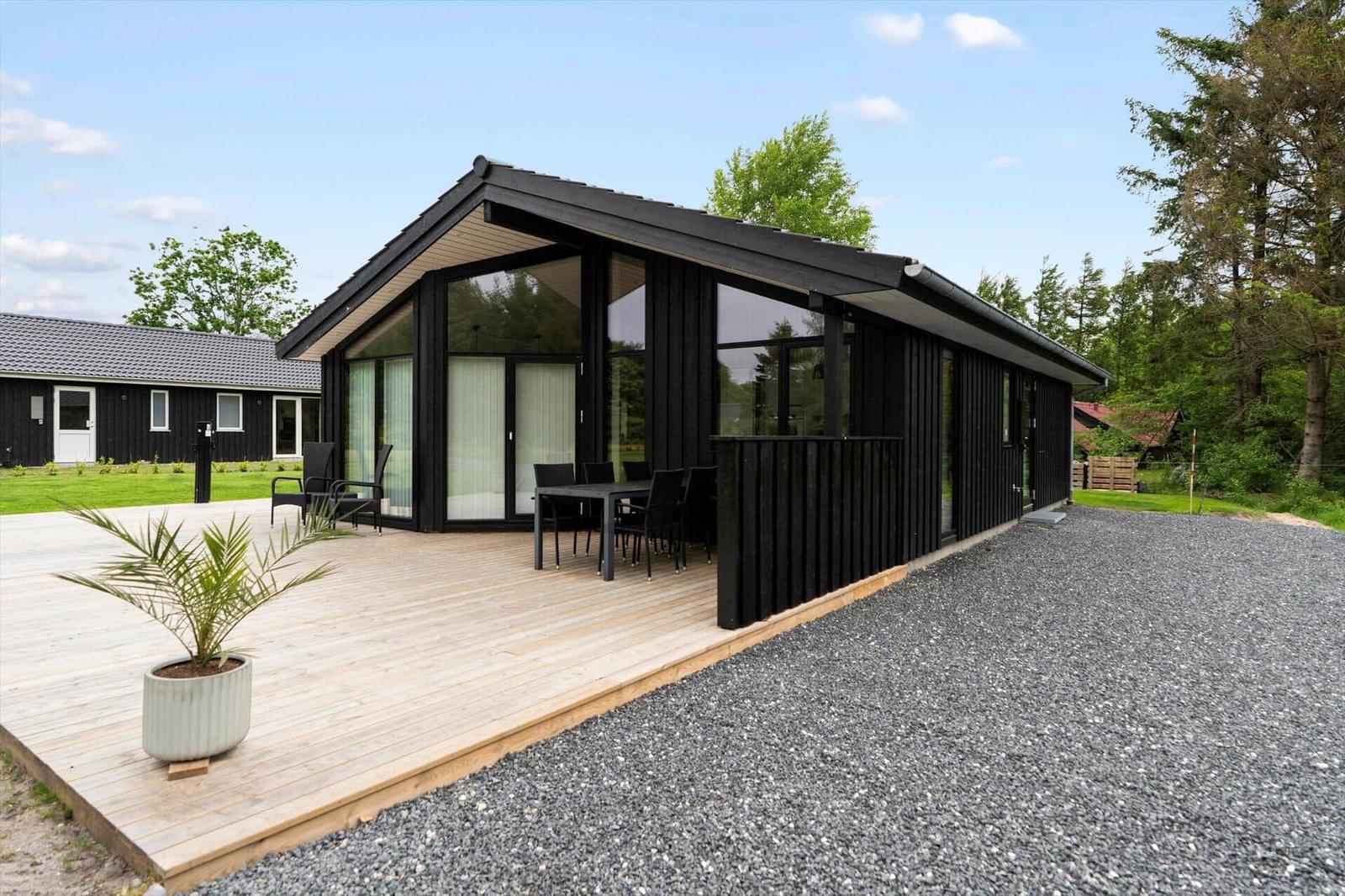 Modern wooden cabin with large deck, garden, and barbecue area.