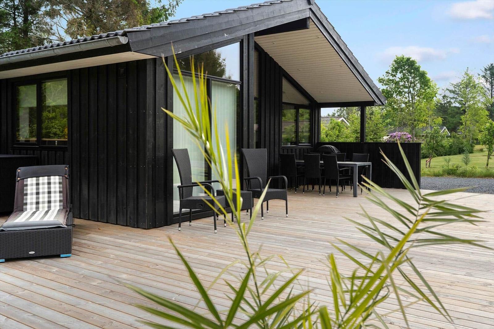 Wooden terrace with seating area in front of modern house with large window area.