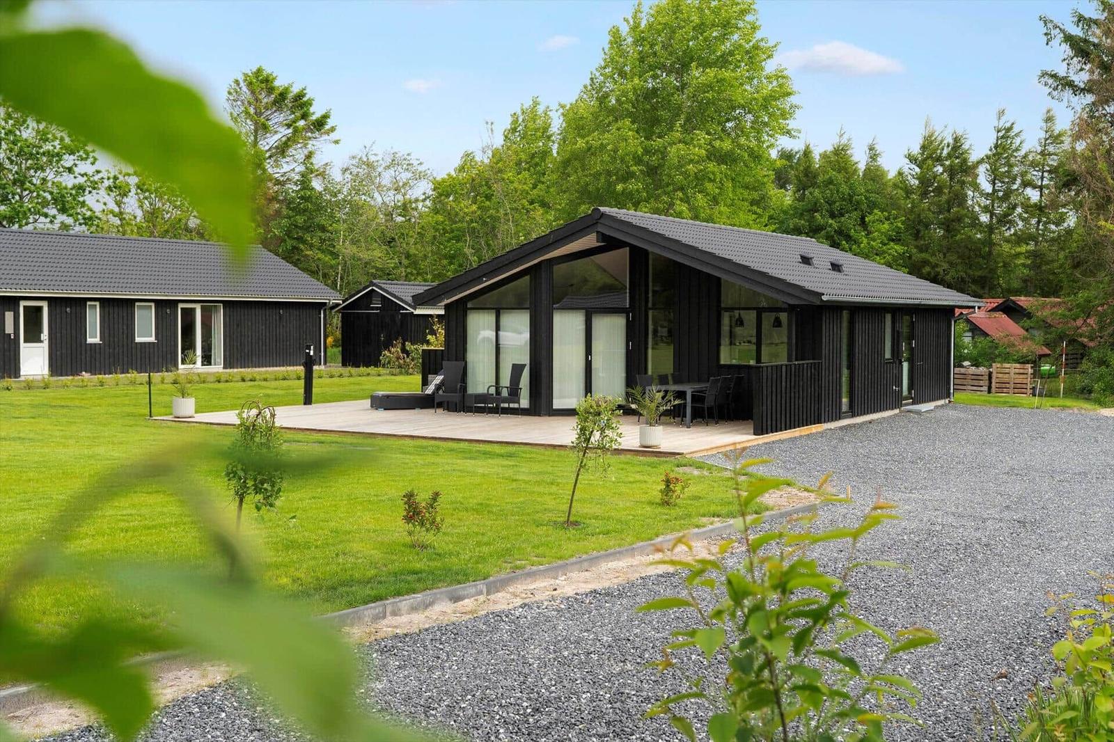 Modern wooden cabin with terrace and garden. Surrounded by trees and grass.