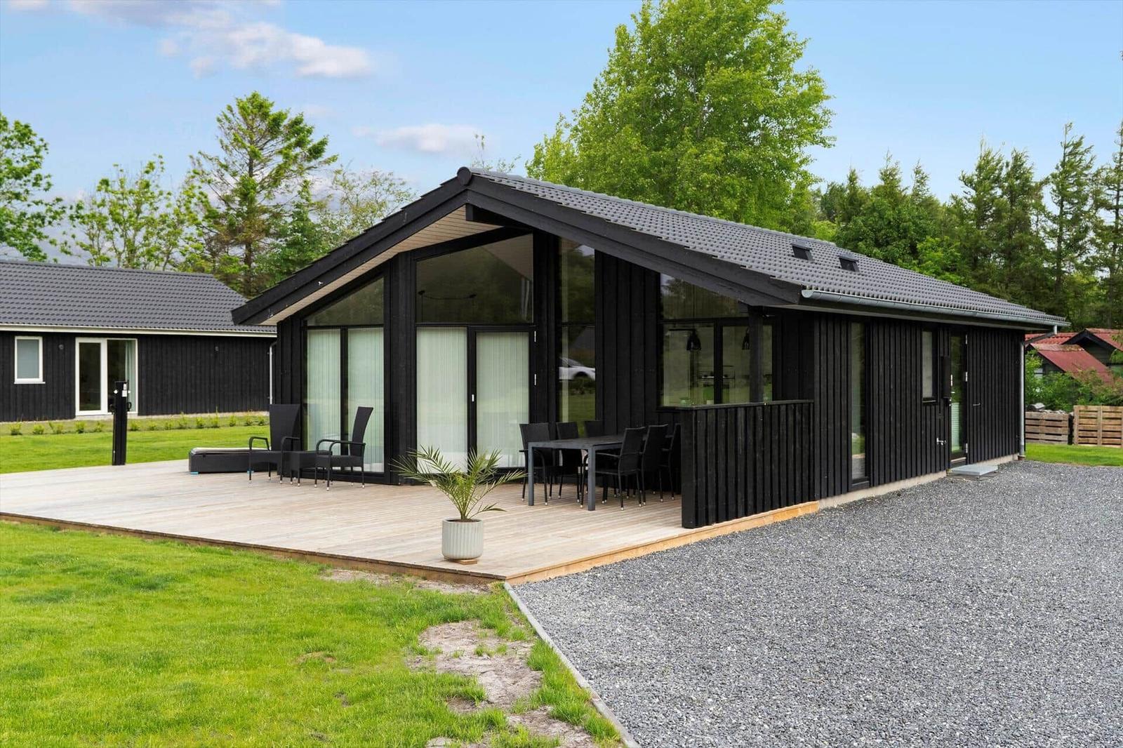 Modern black cabin with terrace, garden, and view of forest.