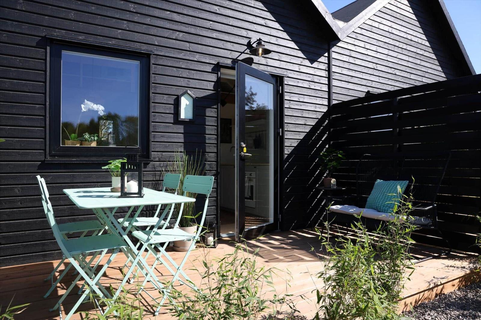 Terrace with table, chairs, and swing in front of black wooden house