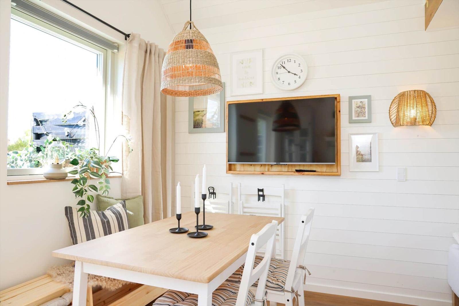 Dining room with wooden table, white chairs, and wall-mounted TV. Clock and pictures on the wall.