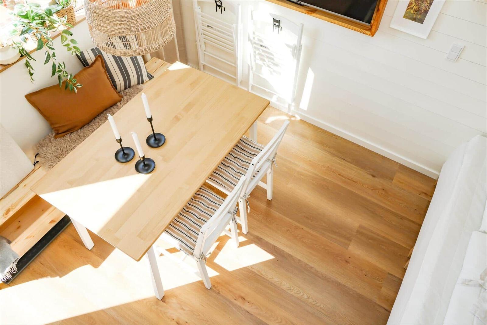 Dining area with wooden table, chairs, and candles. Wall with TV and plant.